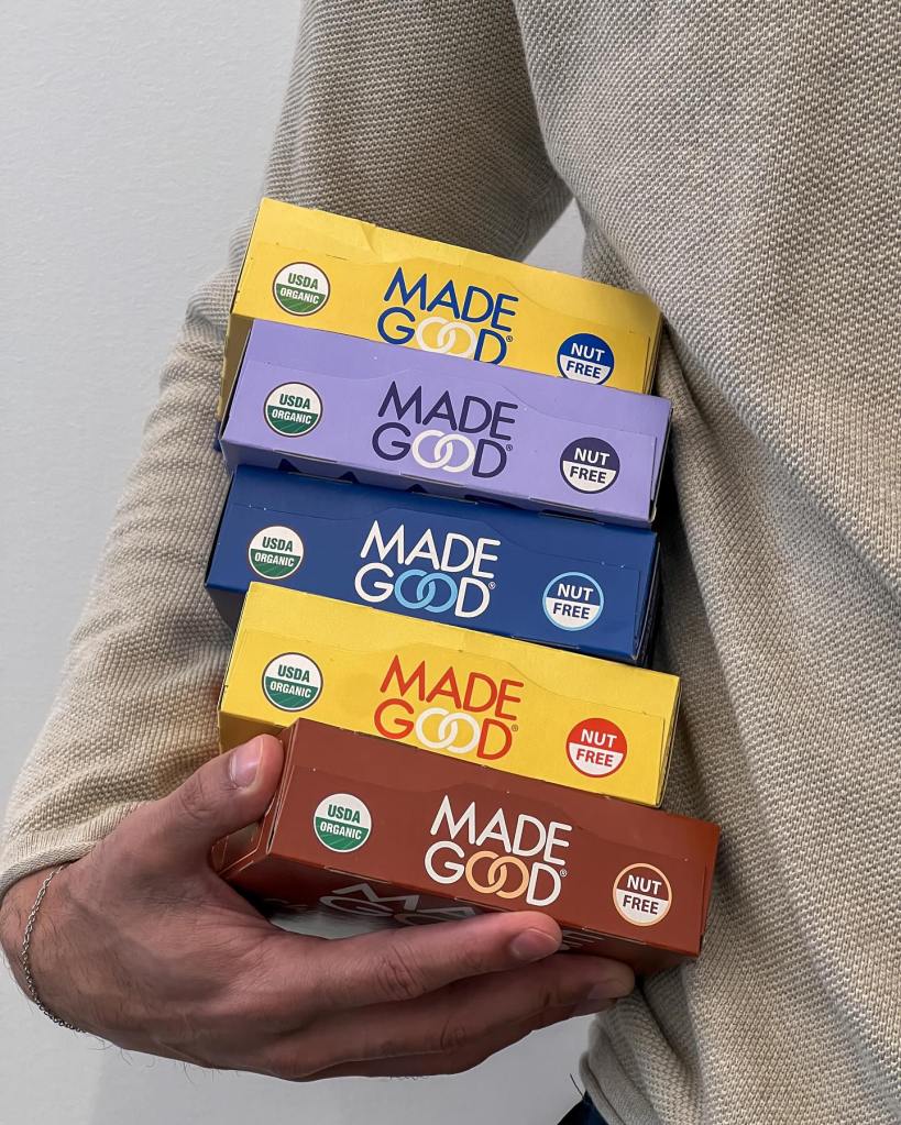A person holding a stack of colored Granola Madegood Granola boxes.