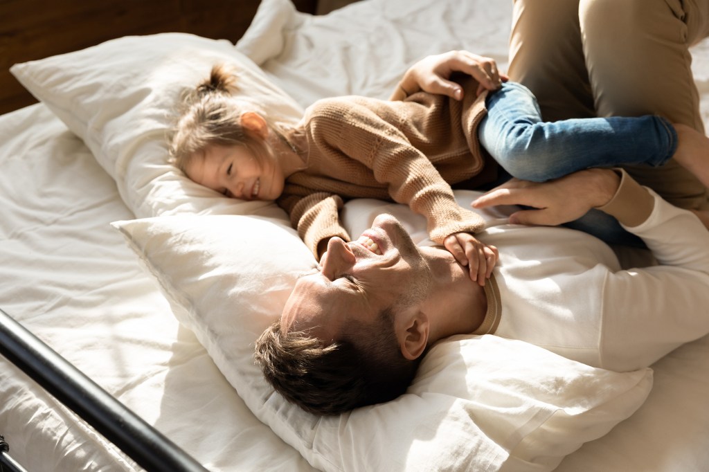 Happy father and little girl resting in bed cozy together, smiling dad having fun with a delightful preschool girl, resting, taking nap in the bedroom,